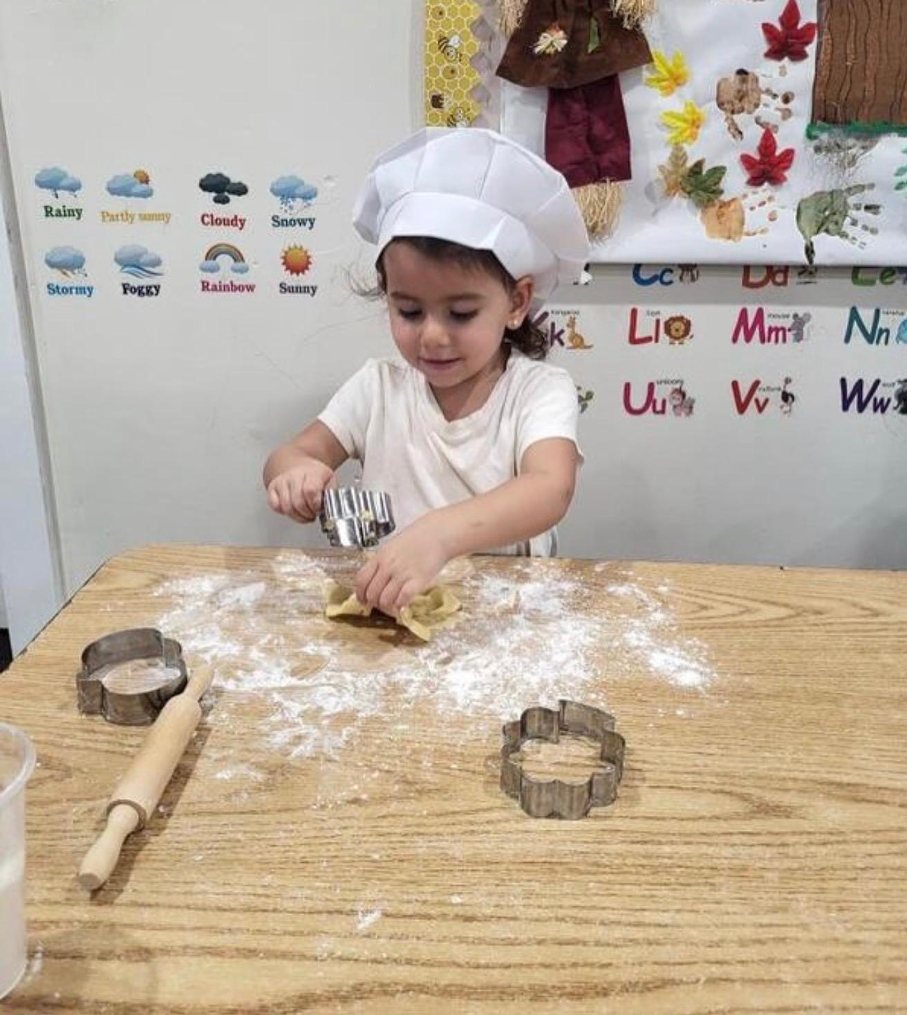 A little baker in a chef hat cutting out dough