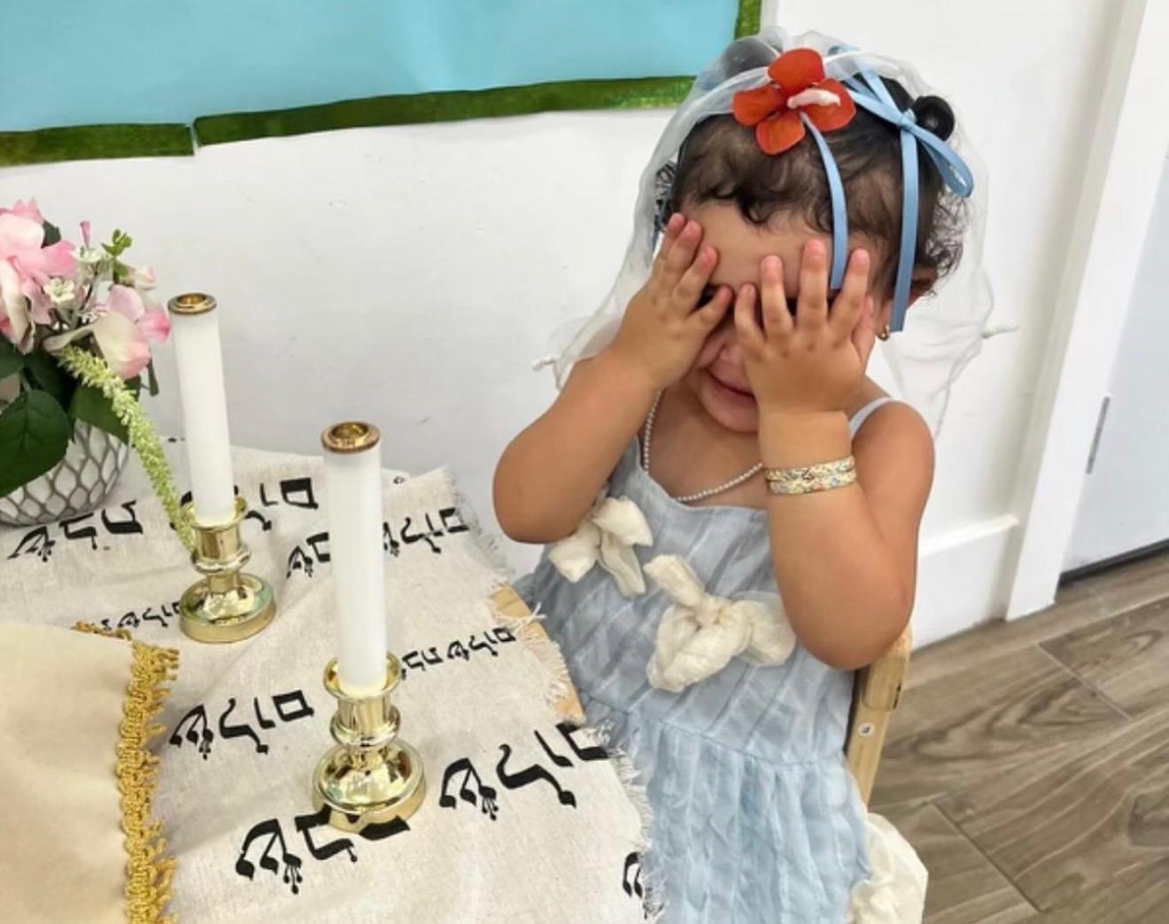 A child covering her eyes for the Shabbat candle blessing